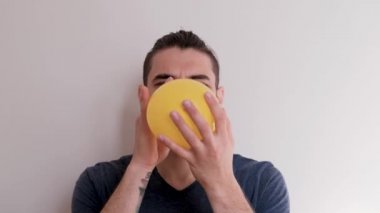 Sarı bir balonu ağızla şişir ve sonra uçup gitmesine izin ver. Sakallı, at kuyruklu, beyaz atlı, beyaz saçlı, genç, beyaz Avrupalı bir adam balonu arka planda şişiriyor..