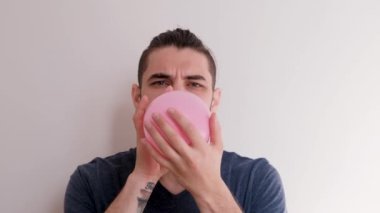 Ağzınla pembe bir balon şişir ve sonra uçup gitmesine izin ver. Sakallı, at kuyruklu, beyaz atlı, beyaz saçlı, genç, beyaz Avrupalı bir adam balonu arka planda şişiriyor..