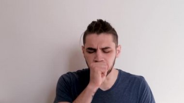 Genç beyaz adam avucunun içinde öksürüyor, burnunu kağıt peçeteye sümürüyor ve kendini çok hasta hissediyor..