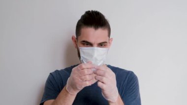 Mavi tişörtlü, tıbbi koruyucu maskeli, beyaz lateks eldivenli beyaz arka planda duran ve şırıngayı ilaçla dolduran beyaz bir beyaz öğrenci. Adam iğneyi yapacak..