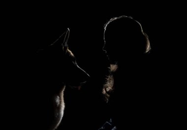 Alman çoban köpeği ve sahibinin profili oturup birbirine bakar. Kız ve evcil hayvan siluetleri çok güzel çizilmiş. Siyah arka plandaki parlak ışıkla aydınlatılmış köpek ve kadın silueti..