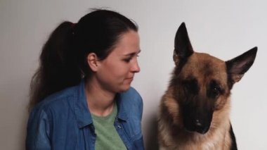 Young pretty girl of Caucasian European appearance kisses her German Shepherd dog. Woman and dog on white background sit close and love each other. Warm relationship between person and pet.