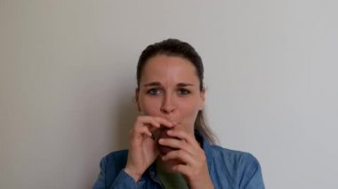 Girl is preparing for holiday and blowing balloon and then lets it fly away. Young pretty woman of Caucasian European appearance inflates burgundy balloon with her mouth on white background.