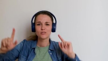 Young pretty Caucasian European woman listens to music with headphones and dances merrily waving her hands to sides. Girl listens to music completely immersed and dissolved in moment catches rhythm.