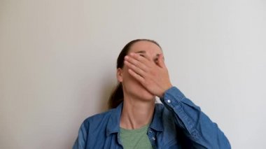 Young Caucasian European girl in shirt sits on white background and drinks pills with water. Treatment with medications and antibiotics at home. 4K footage of taking tablets by person.