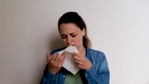 白い背景の若い白人ヨーロッパ人女性が彼女の手に咳をし その後 白い紙ナプキンに彼女の鼻を吹く 病気の女の子は痛みを感じている 4K映像 — ストック動画
