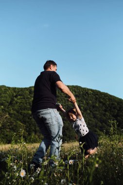 Babalar Günü 'nde birlikte vakit geçirin. Genç beyaz bir baba kızını kollarına alır ve neşeyle güler. Papatya tarlasında kızla bir adam gün batımında.