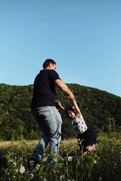 Babalar Günü 'nde birlikte vakit geçirin. Genç beyaz bir baba kızını kollarına alır ve neşeyle güler. Papatya tarlasında kızla bir adam gün batımında.