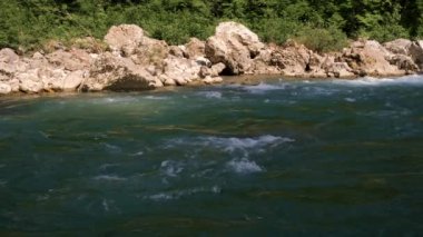 Yatay 4k video yavaş çekim. Mavimsi renkte güzel, fırtınalı bir dağ nehri büyük taşların arasında. Arka planda yoğun yeşil yaprak döken orman.