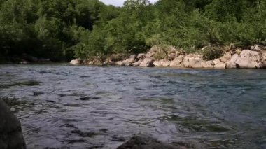 Yatay yakınlaştırma 4K yavaş çekim videosu. Mavimsi renkte güzel, fırtınalı bir dağ nehri büyük taşların arasında. Arka planda yoğun yeşil yaprak döken orman.