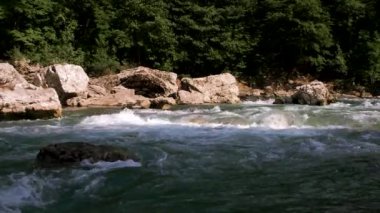 Yatay yakınlaştırma 4K yavaş çekim videosu. Mavimsi renkte güzel, fırtınalı bir dağ nehri büyük taşların arasında. Arka planda yoğun yeşil yaprak döken orman.