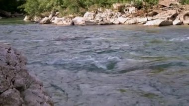 Yatay yakınlaştırma 4K yavaş çekim videosu. Mavimsi renkte güzel, fırtınalı bir dağ nehri büyük taşların arasında. Arka planda yoğun yeşil yaprak döken orman.