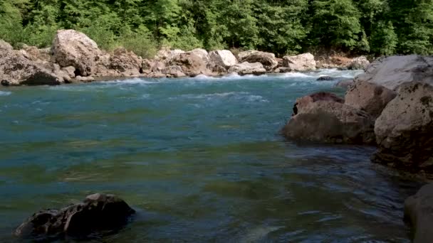 水平4Kビデオスローモーション 大きな石の間で峡谷の青みがかった色合いの美しい嵐の山の川 背景に濃い緑の落葉樹林 — ストック動画