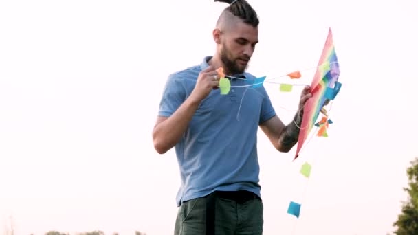 Lgbtの旗凧 スローモーション4Kビデオ 若いです白人男性とドレッドロックは立っているとそれを起動し 新鮮な空気中で楽しみを持っているために絡み合う凧をしようとしています — ストック動画