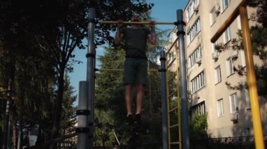 Açık alanda spor aktiviteleri ve sağlıklı yaşam tarzı. Kol kasları için spor ve güç egzersizleri. Sakallı kaslı beyaz adam iki eliyle yatay çizginin üzerine çıkıyor..