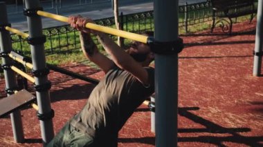 Kafkasyalı adam iki eliyle aşağıdan yatay çubuğa tırmanıyor. Açık alanda spor aktiviteleri ve sağlıklı yaşam tarzı. Kollar için spor ve güç egzersizleri. Eğitimden önce ısın..
