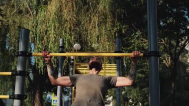 Kafkasyalı adam iki eliyle aşağıdan yatay çubuğa tırmanıyor. Açık alanda spor aktiviteleri ve sağlıklı yaşam tarzı. Kollar için spor ve güç egzersizleri. Eğitimden önce ısın..