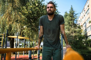 Genç yakışıklı beyaz adam sıcak bir yaz sabahı kendini sokak sporları sahasına atıyor. Yatay paralel çubuklardaki kol kasları için güç eğitimi. Etkin yaşam tarzı kavramı.