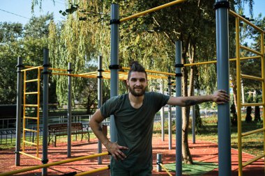 Genç adam donanımlı açık hava egzersiz alanında duruyor ve dinleniyor. Erkek fitness eğitmeniyle pankart. Güç eğitiminden önce güç ve enerji depoluyor. Etkin yaşam tarzı kavramı.