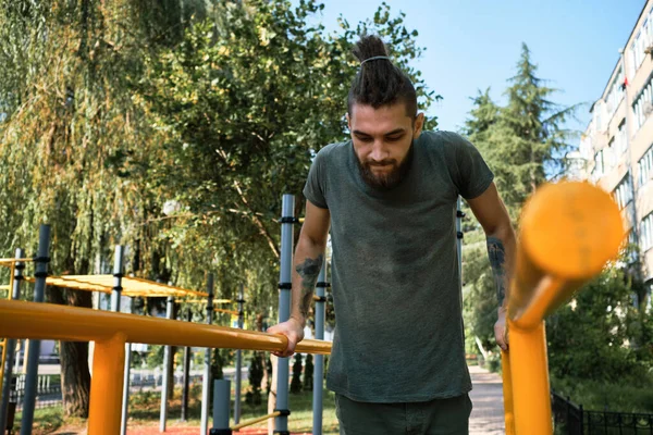 Genç yakışıklı beyaz adam sıcak bir yaz sabahı kendini sokak sporları sahasına atıyor. Yatay paralel çubuklardaki kol kasları için güç eğitimi. Etkin yaşam tarzı kavramı.