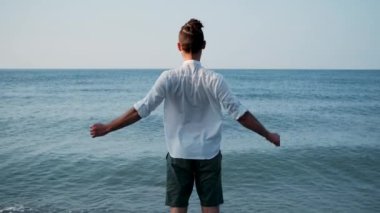 Beyaz gömlekli beyaz adam sakin mavi denizin arka planında duruyor ve esniyor. Nefesini ve bedenini hisset ve düşüncelerden arındır. Ilık yaz sabahında ısınırız. Kollarını uzat..
