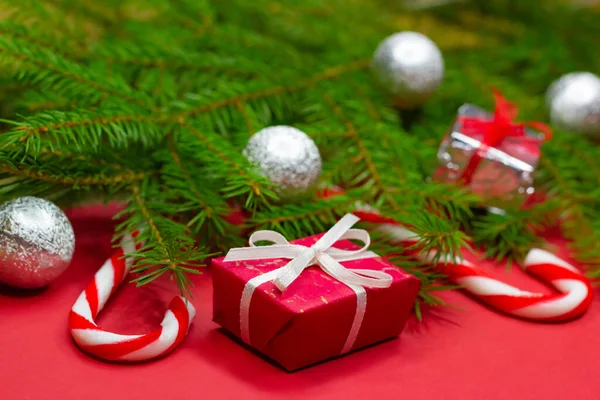 Primer plano de las ramas del árbol de Navidad decoradas con cajas de regalo, bolas de Navidad y bastones de caramelo sobre fondo rojo — Foto de Stock