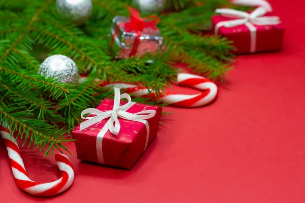 Primer plano de las ramas del árbol de Navidad decoradas con cajas de regalo, bolas de Navidad y bastones de caramelo sobre fondo rojo con espacio de copia. — Foto de Stock