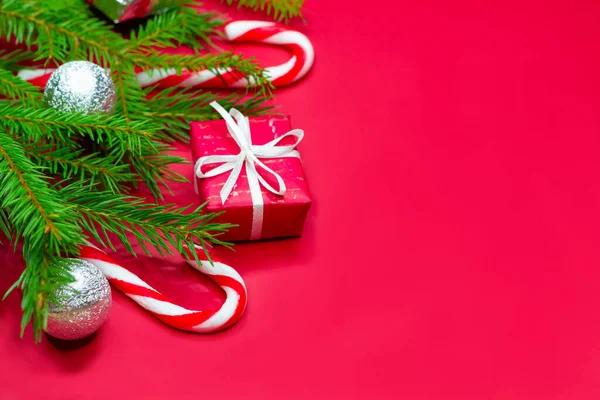 Primer plano de las ramas del árbol de Navidad decoradas con cajas de regalo, bolas de Navidad y bastones de caramelo sobre fondo rojo con espacio de copia. — Foto de Stock