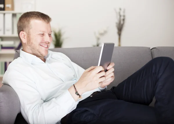 Mann lächelt glücklich, als er sein Tablet liest — Stockfoto