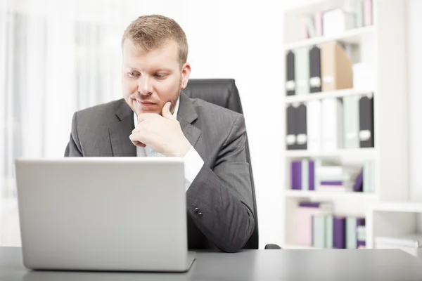 Mann blickt mit verschmitztem Gesichtsausdruck auf seinen Laptop — Stockfoto
