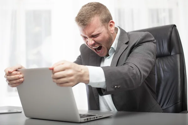 Homem de negócios irritado sacudindo seu computador portátil — Fotografia de Stock