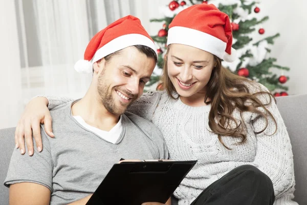 Happy couple write list for christmas on sofa — Stock Photo, Image