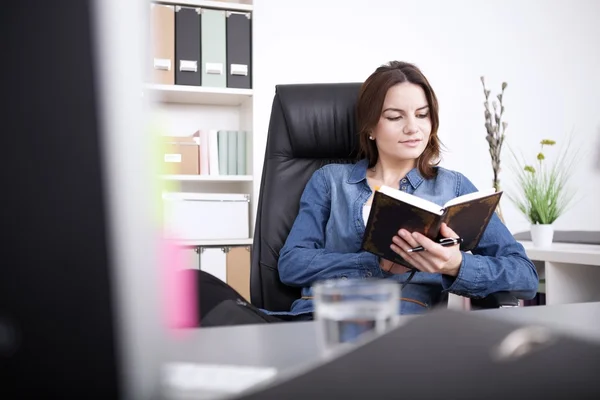 Bürofrau liest ein Buch, während sie auf dem Stuhl sitzt — Stockfoto