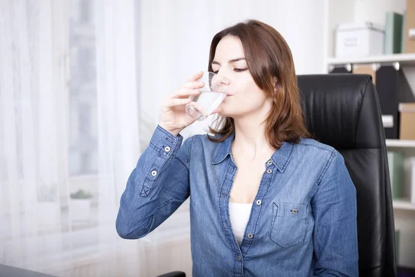 Frau sitzt auf Bürostuhl und trinkt Wasser — Stockfoto