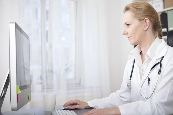 Kvinnliga läkare vid hennes skrivbord med hennes dator — Stockfoto