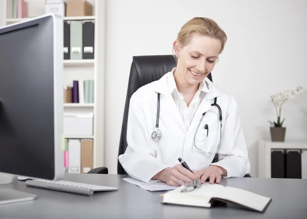 Happy Woman Doctor fazendo relatórios médicos na tabela — Fotografia de Stock