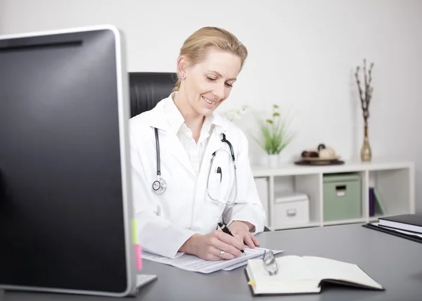 Feliz doctora escribiendo hallazgos médicos en su mesa — Foto de Stock