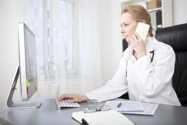 Female Doctor Calling Phone While Using Computer — Stock Photo, Image