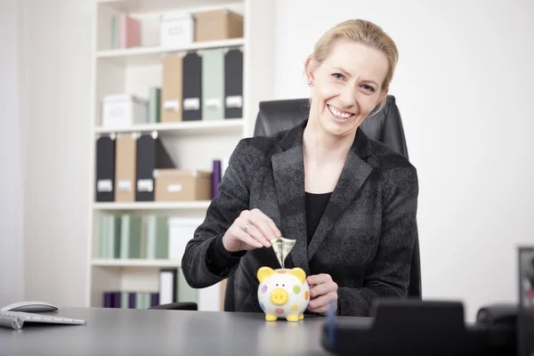 Glückliche Geschäftsfrau legt Geld aufs Sparschwein — Stockfoto