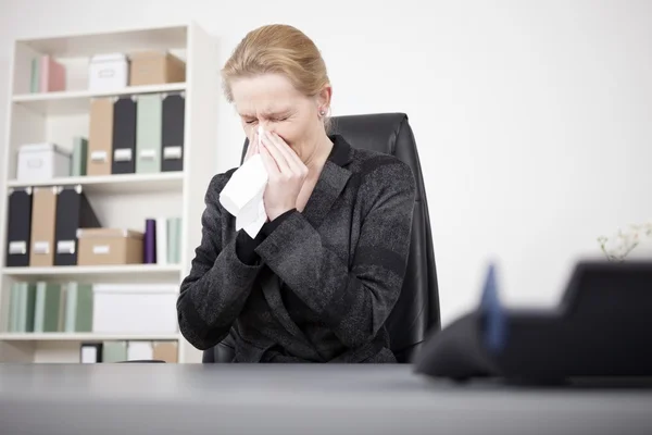 Managerin niest mit geschlossenen Augen in ihrem Büro — Stockfoto