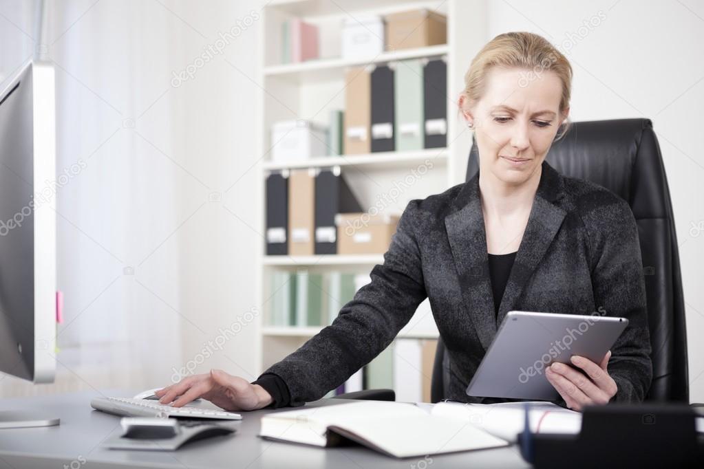 Manageress with Tablet Typing on Desktop Computer