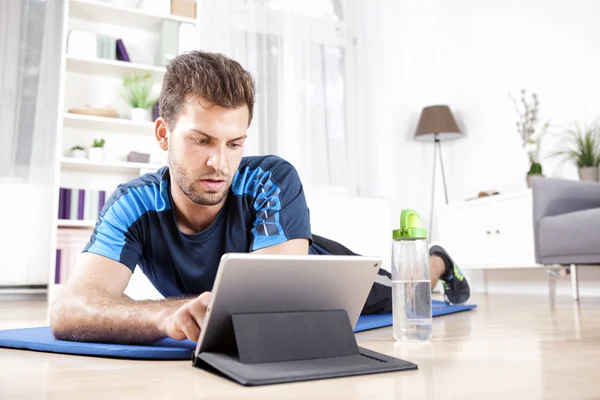 Beau mec avec tablette ordinateur couché sur un tapis — Photo