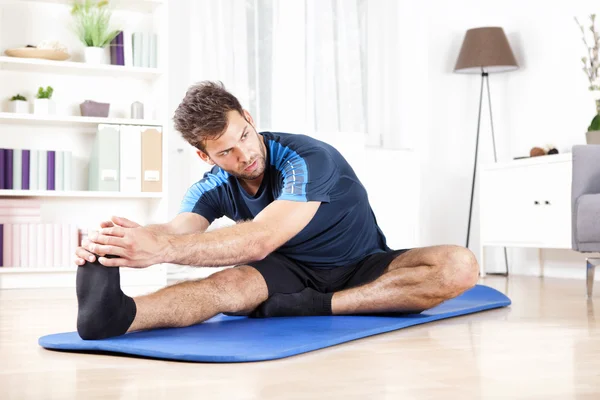 Precioso hombre realizando isquiotibial estiramiento en casa —  Fotos de Stock