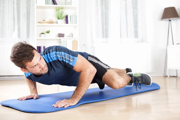 Uomo in forma planking su stuoia mentre solleva una gamba — Foto Stock