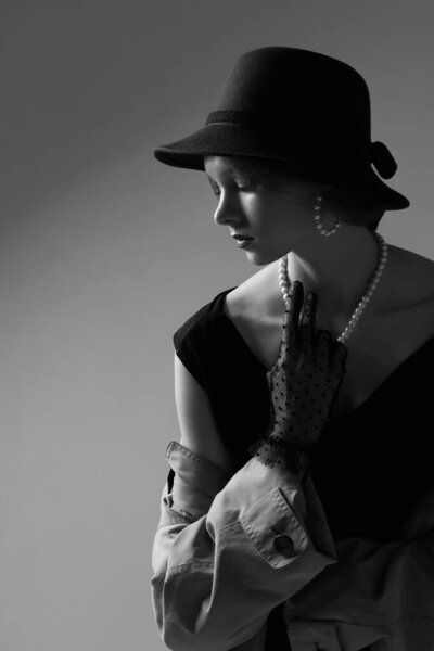 High fashion portrait of elegant woman in retro look. Black and white image, hat, dress, coat, necklace