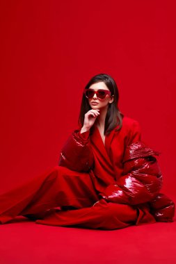 Kırmızı takım elbiseli, ceketli ve güneş gözlüklü manken. Stüdyo çekimi.