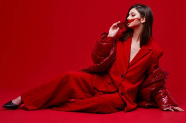 Kırmızı takım elbiseli, ceketli ve güneş gözlüklü manken. Stüdyo çekimi.