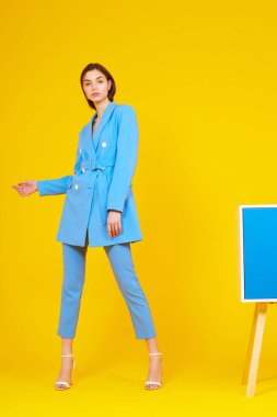 Mavi takım elbiseli zarif bir kadının yüksek moda portresi. Sarı arkaplan, stüdyo çekimi