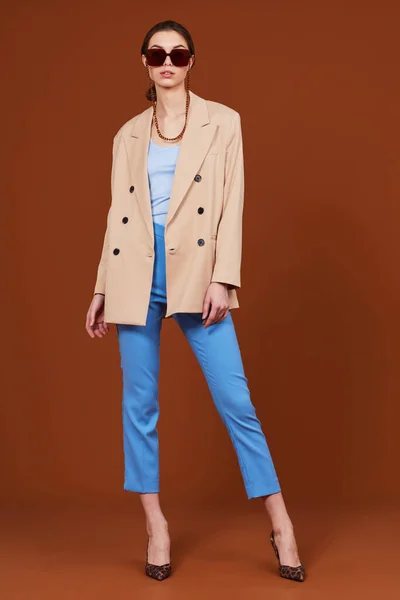 ベージュのジャケットとジーンズで若いエレガントな女性の高いファッションの肖像画 サングラス 茶色の背景 スタジオショット — ストック写真