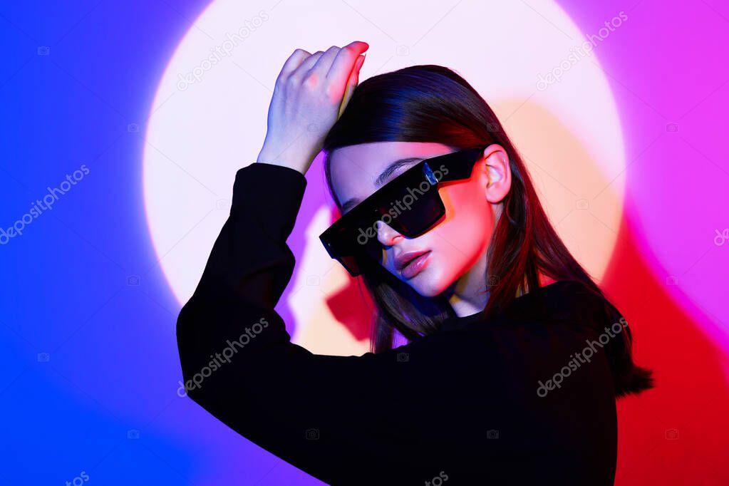 Fashion portrait of young elegant woman in trendy sunglasses. Neon light, studio shot